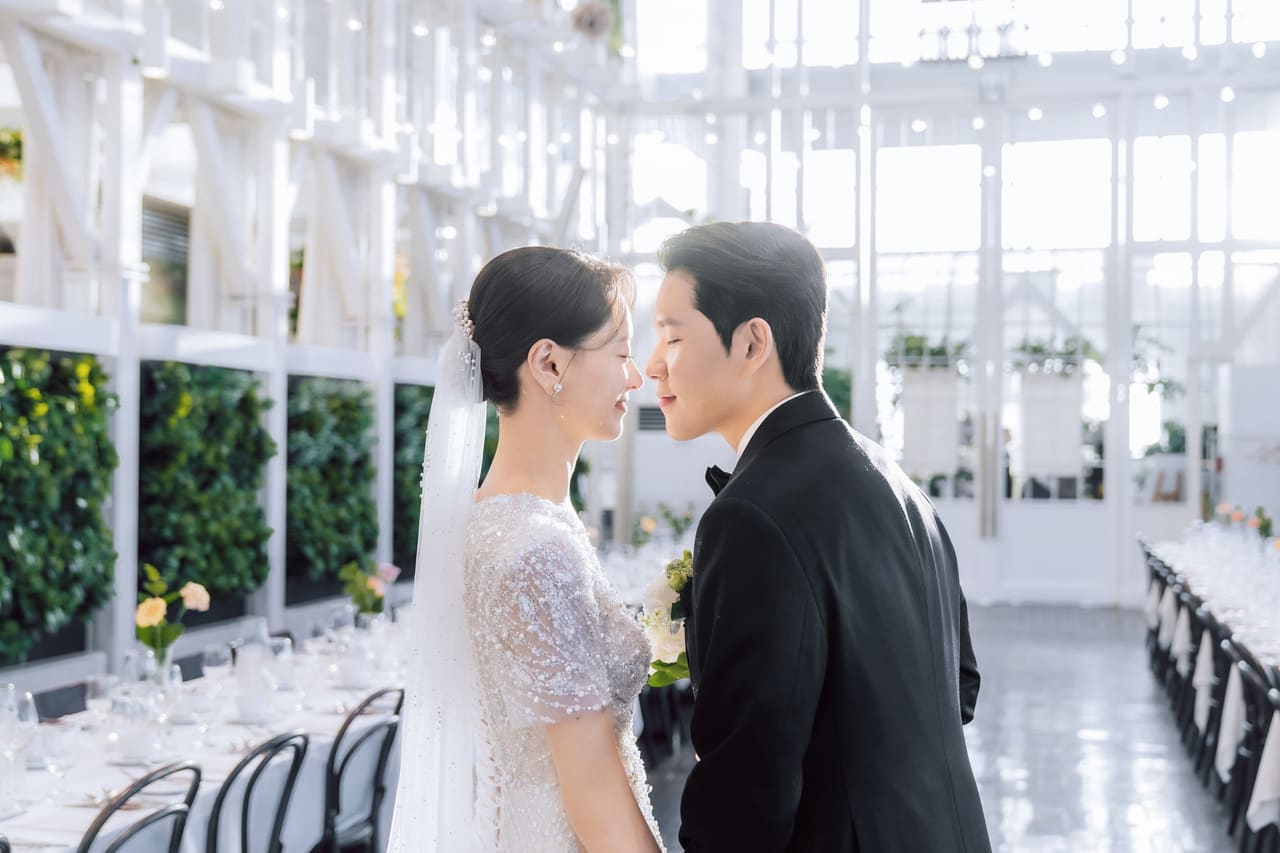 화이트 웨딩홀에서 마주 보고 미소 짓는 신랑 신부 본식 스냅